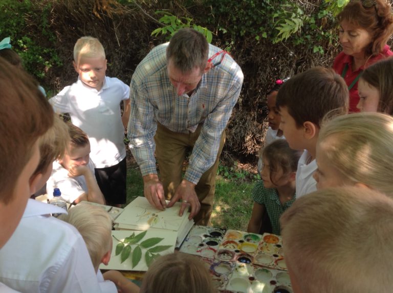 Adult showing children drawing of leaves on paper. Outside on a sunny day.