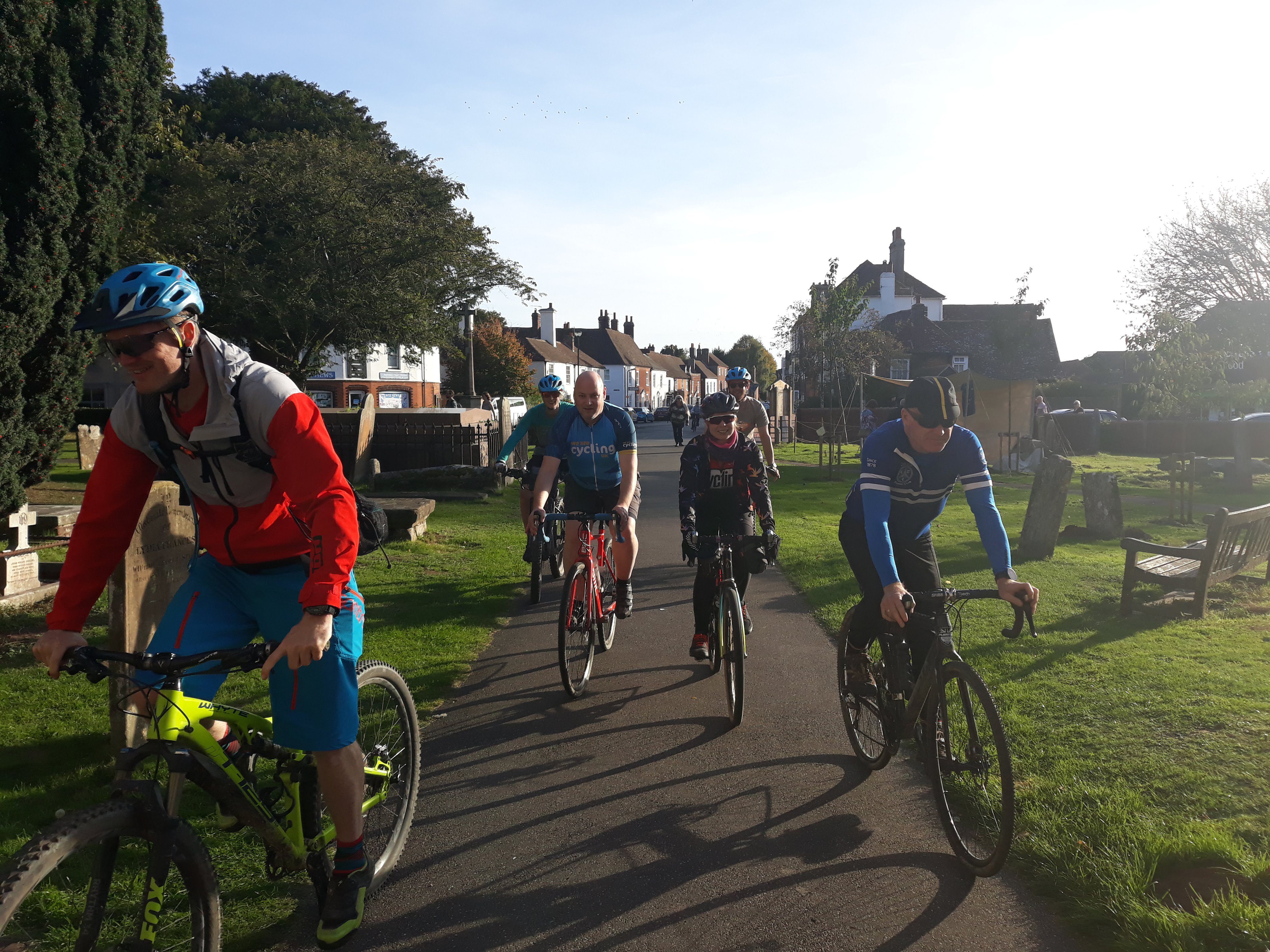 Group of cyclists on path, cycling through church yard, on a sunny day.