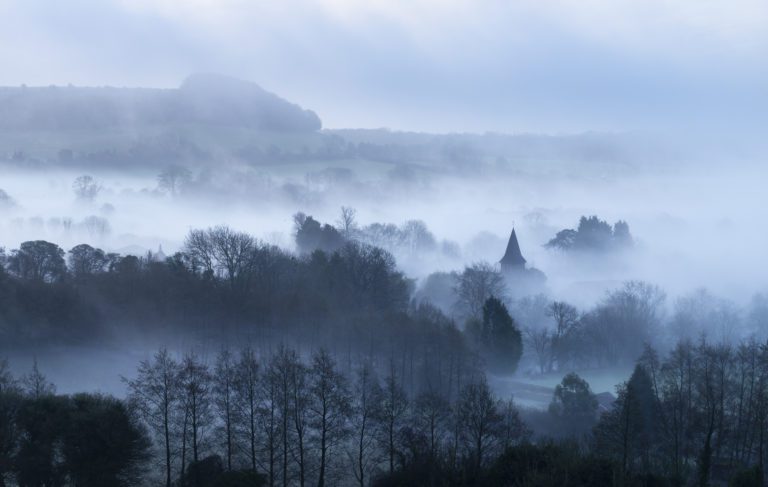 Foggy landscape, with some trees and landmarks showing through the mist.