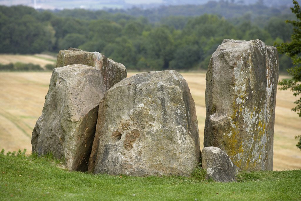 Close-up of Coldrum Stones, on grass with crop fields and woodland in distance.