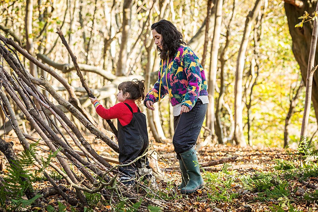 Adult and child building a den outside, in woodland. Using wooden branches.