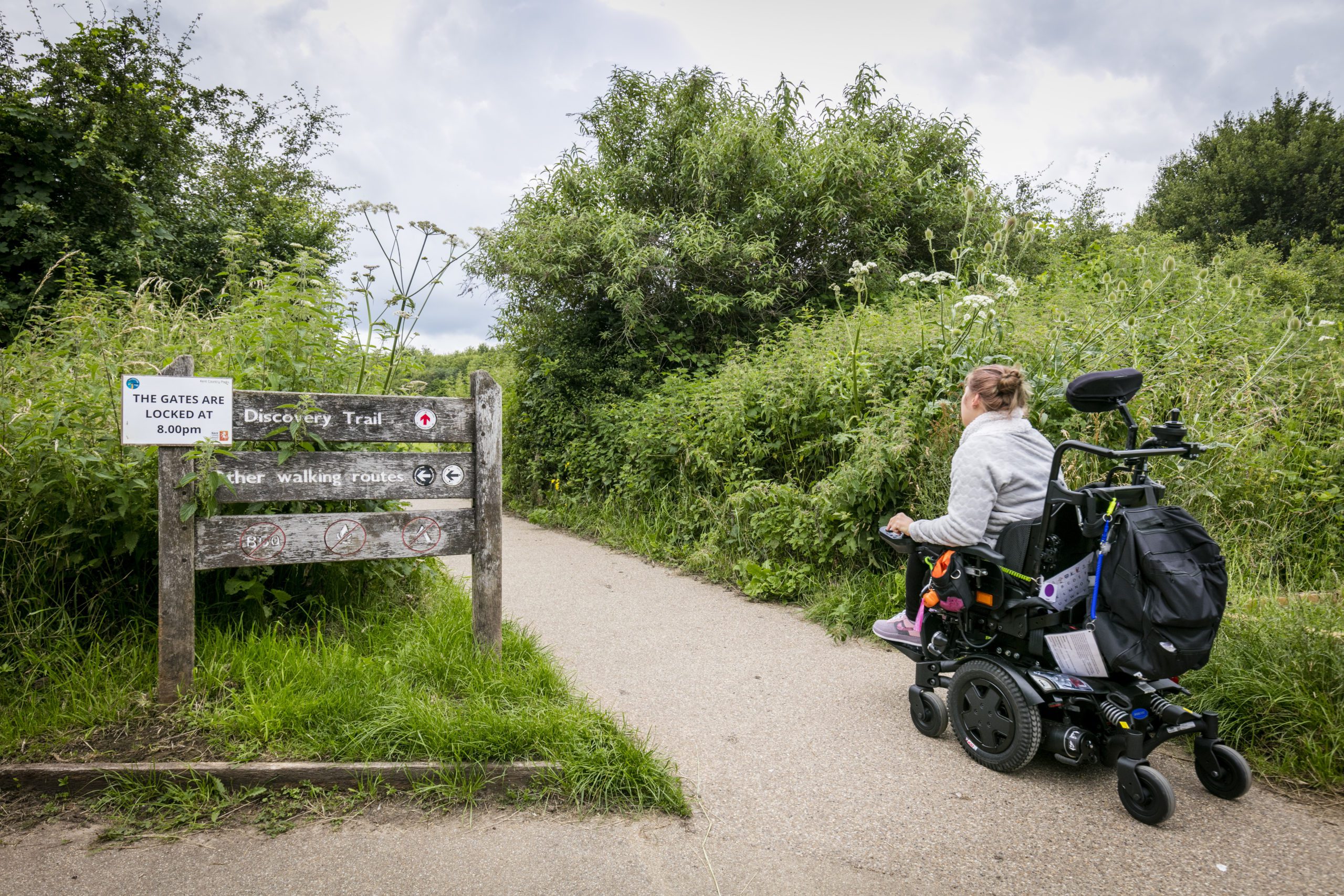 Person on wheelchair at Discovery Trail path, with trees and shrubs around.