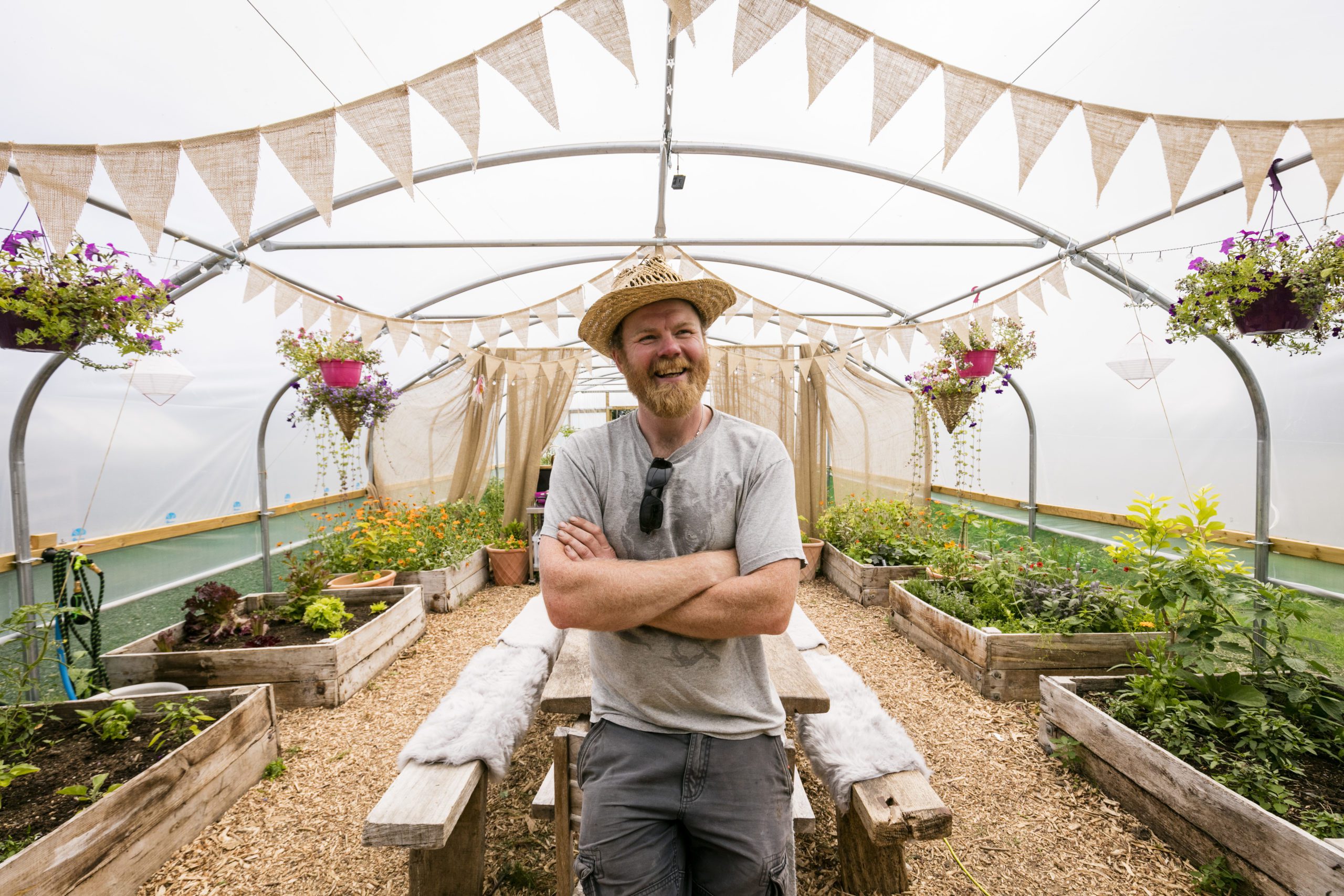 The Rebel Farmer looking at camera, in a polytunnel with bunting and plants.