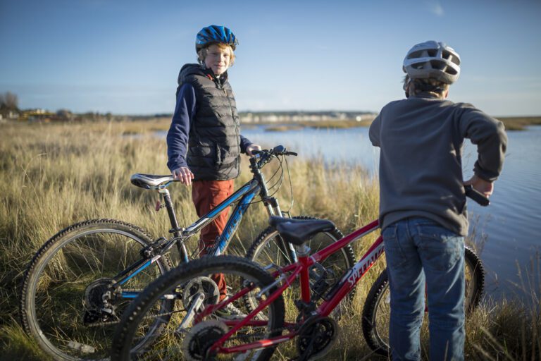 Two older children cycling on the Viking Coastal Trail. Standing and looking at the view.