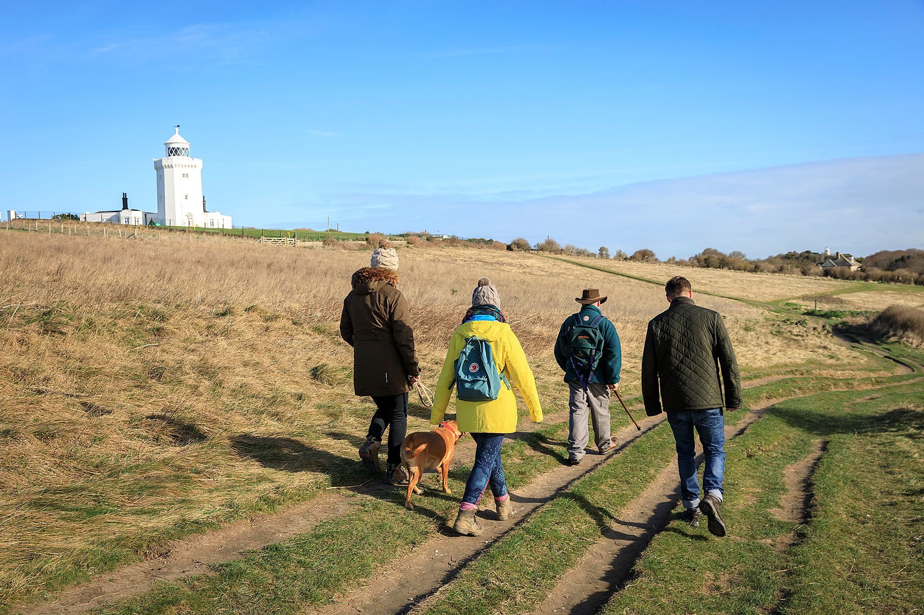 Group of four people walking with dog toward white lighthouse