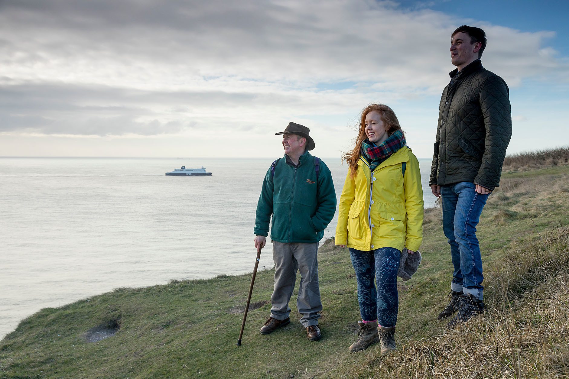 Three people standing at cliff edge looking out to sea