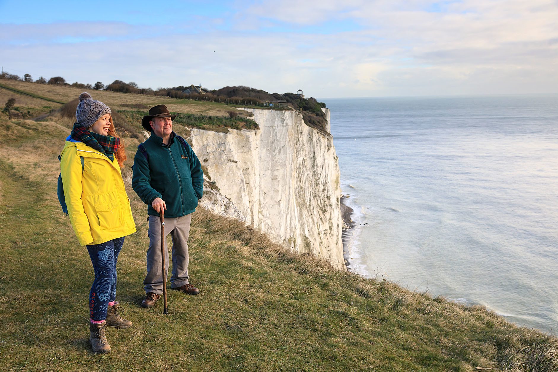Two people standing at cliff edge looking out at the sea