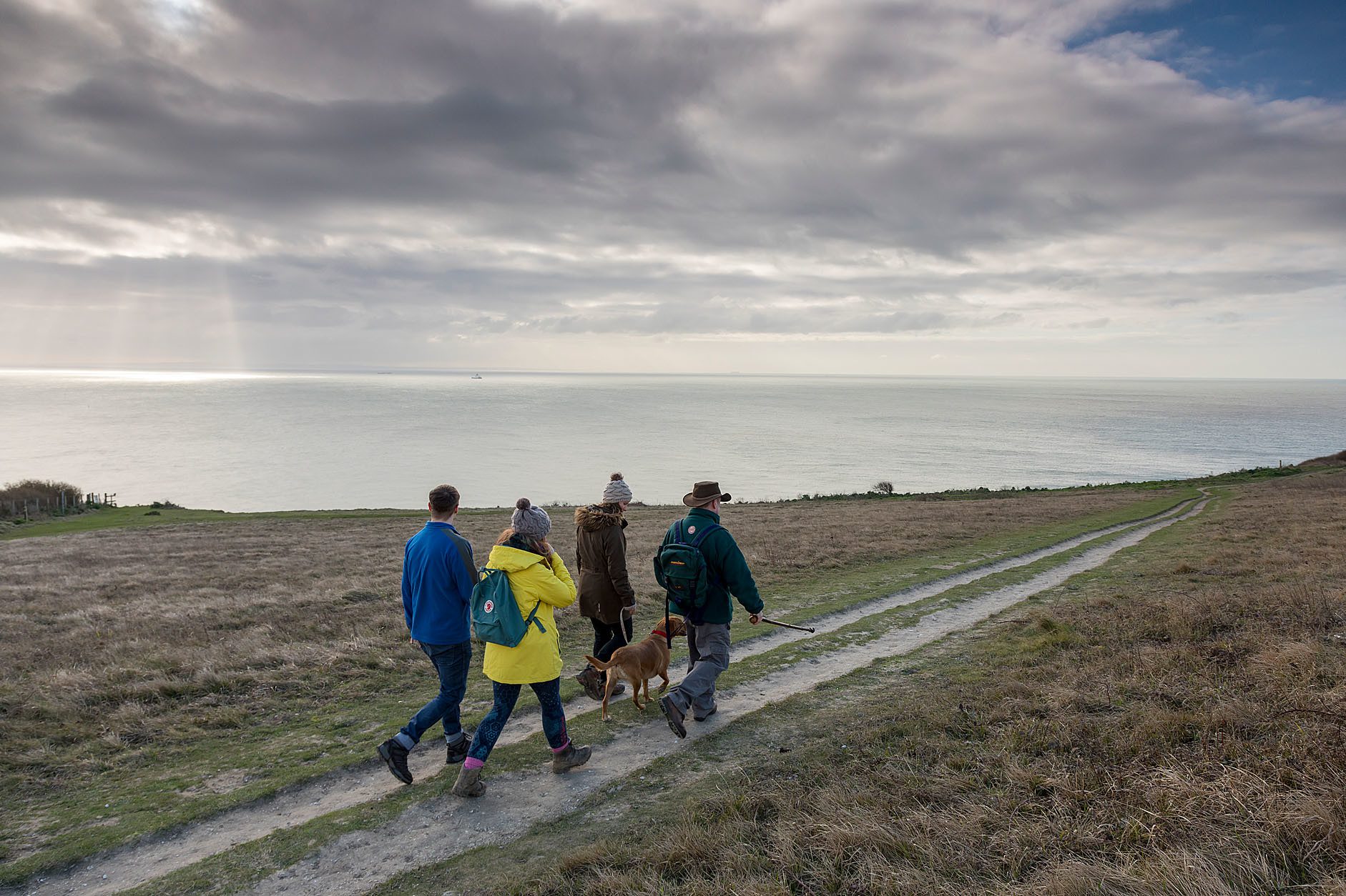 Four people walking dog along cliff top path