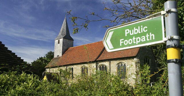 Church nestled in greenery with public footpath sign on the right.