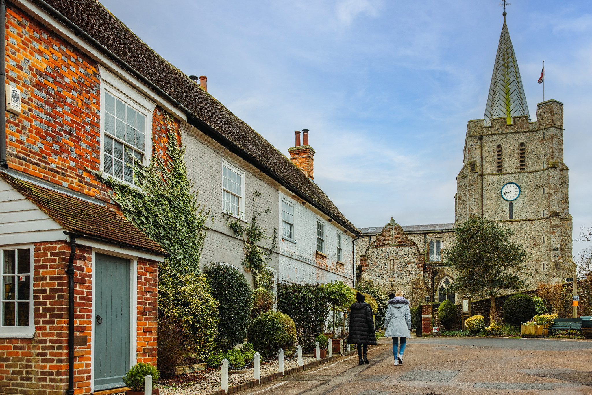 Two people walking towards a village church with houses to the left