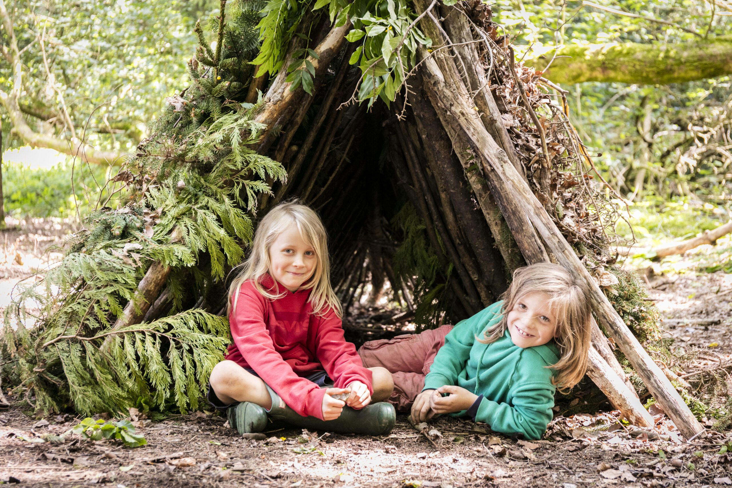 Two children posing in front of teepee made of sticks