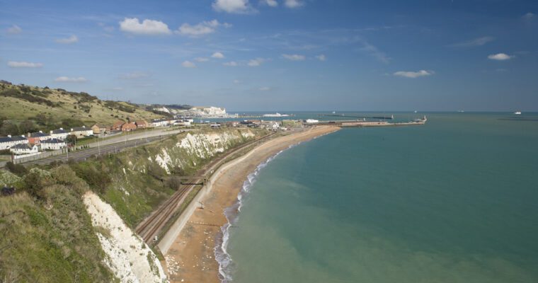 Dover Beach on and sea front a sunny day. Sea on the right, with beach, cliffs and road to the left.