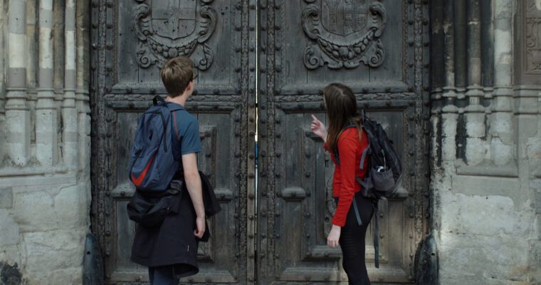 Two people at Canterbury Cathedral door. Big wooden doors with scrolls on.
