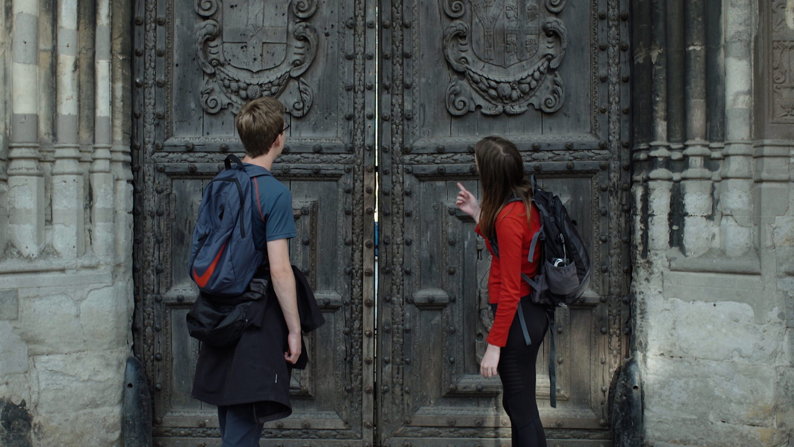 Two people at Canterbury Cathedral door. Big wooden doors with scrolls on.
