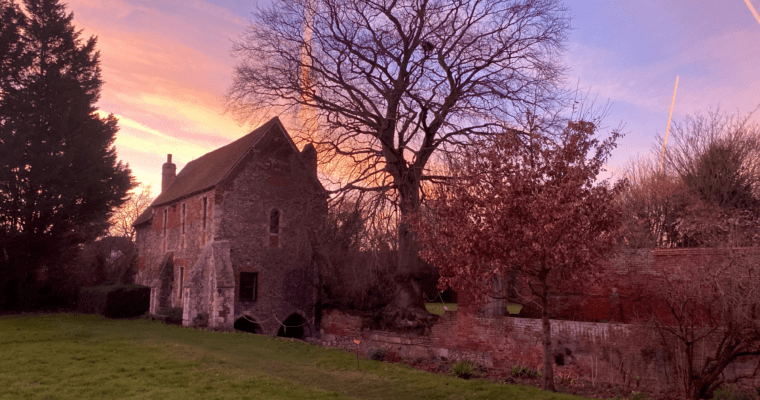 Franciscan Gardens at sunset. Grass, with stone building in the left and some trees surrounding.