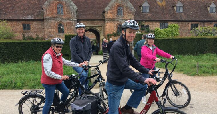Group of people on bikes, looking at camera, outside a country house.