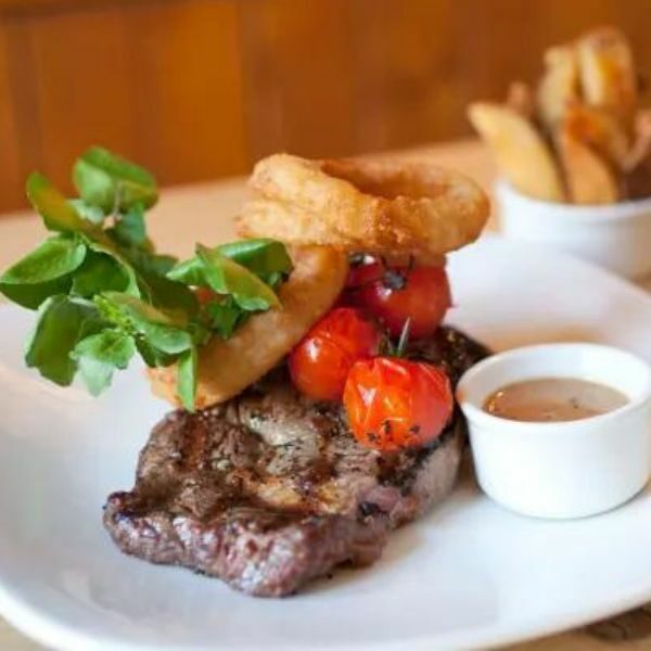 Close-up steak, tomatoes and onion rings on plate.