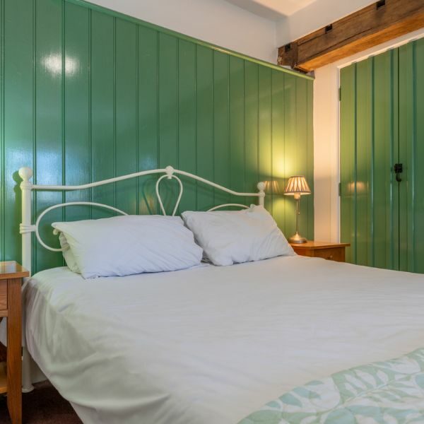 Double bedroom in The Woolpack Hotel. White covers on bed and green walls.