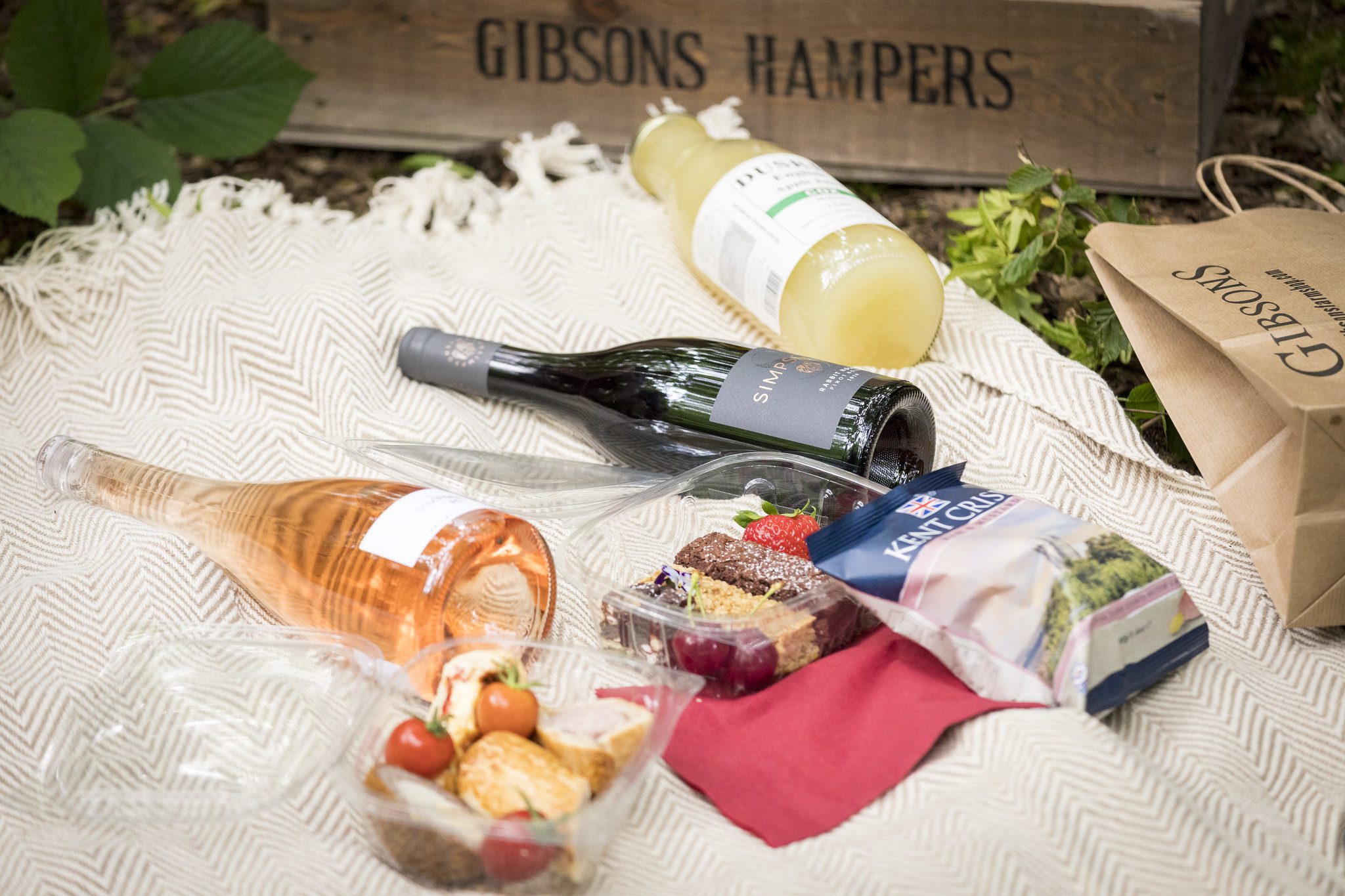 Close-up on picnic blanket with wine, cakes and crisps.