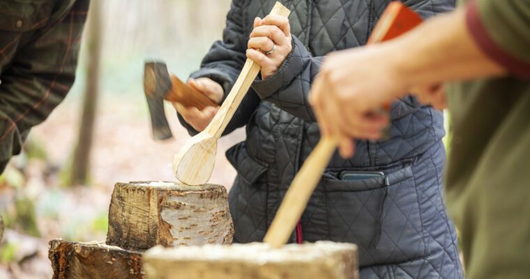 Close-up person with small axe cutting on wooden block to make a spoon.