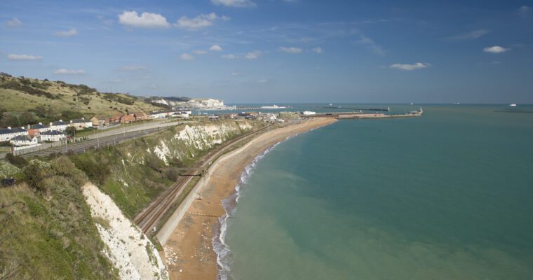 Dover Beach on and sea front a sunny day. Sea on the right, with beach, cliffs and road to the left.