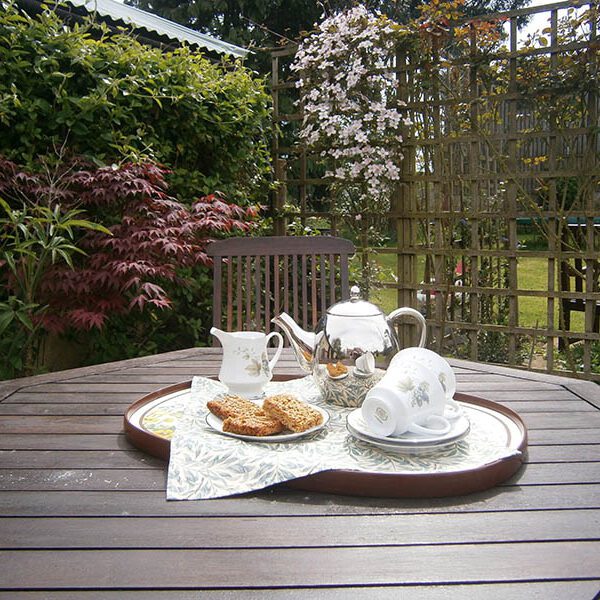 Picnic table with pot of tea and flapjacks. Surrounded with bushes and climbing plants.