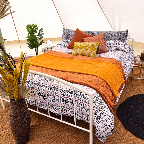 Double bed inside glamping tent with orange and yellow bedding.