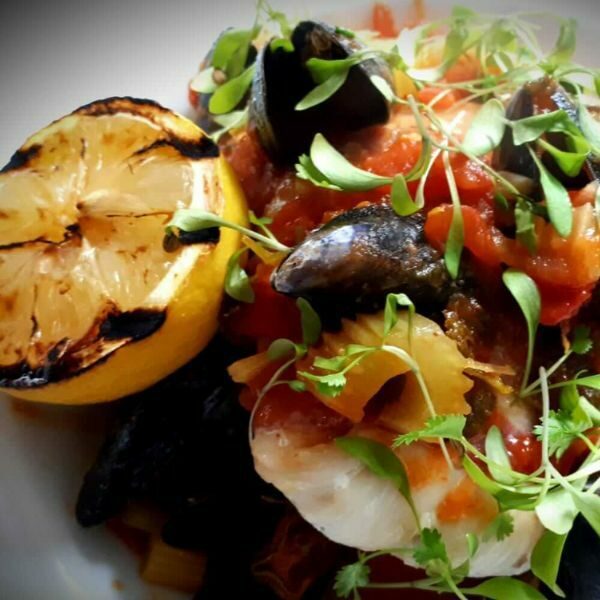 Lemon, moules marinieres, tomatoes and celery on plate.