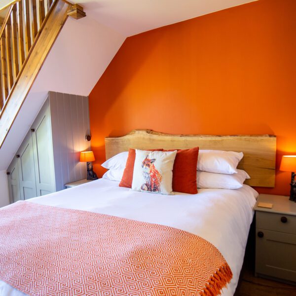 Double bedroom at The Plough Inn, with orange wall and matching bed cover.