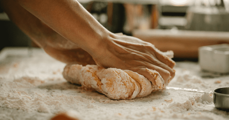 Close-up of a person kneading dough on flour surface.