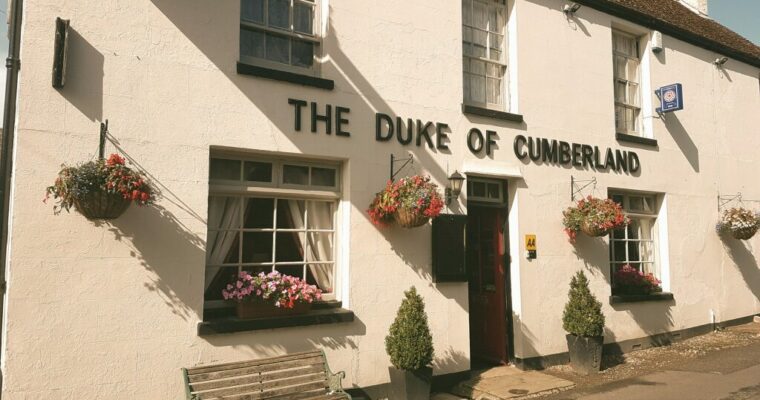 Outside of The Duke of Cumberland pub. White building with bench outside.
