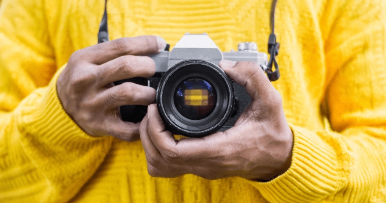 Man holding SLR camera against yellow jumper.