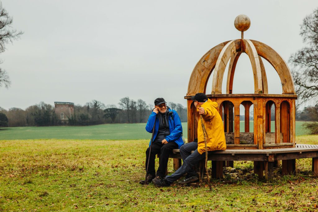 Two people with raincoats sitting on Monumenta Romana sculpture bench.