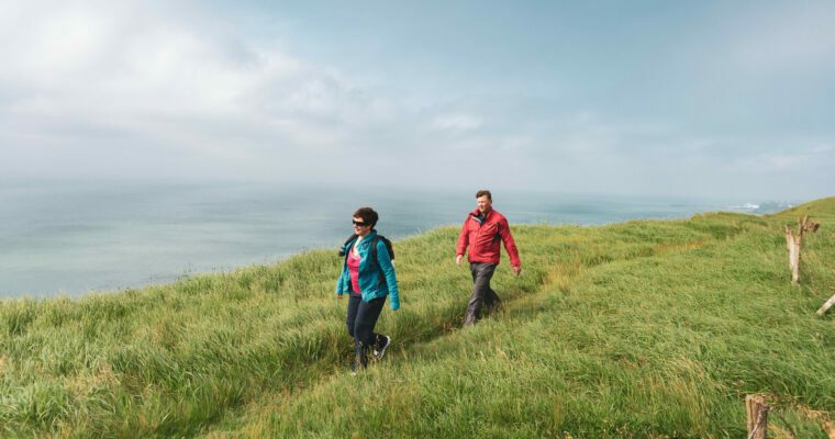 Two people walking on grass cliff top by the sea.