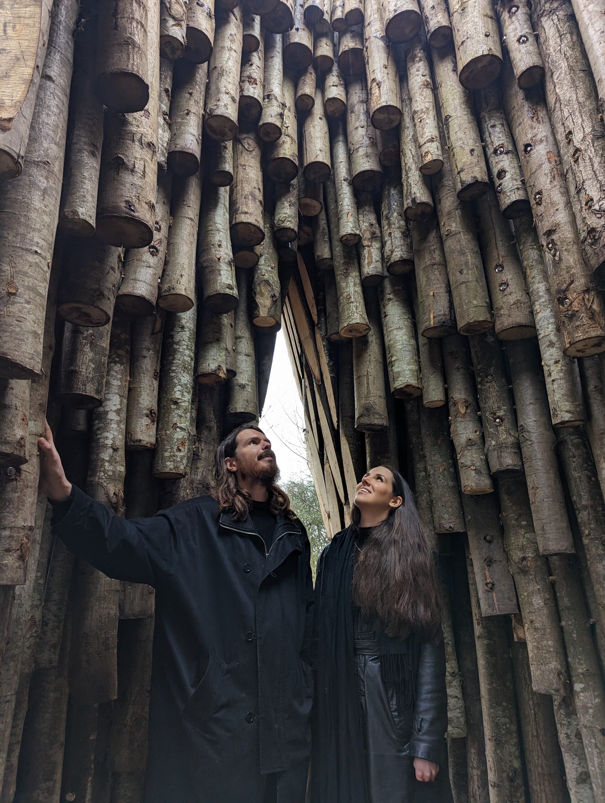 Artists Matthijs and Simone standing inside the wooden coppiced shelter gazing up to the sky
