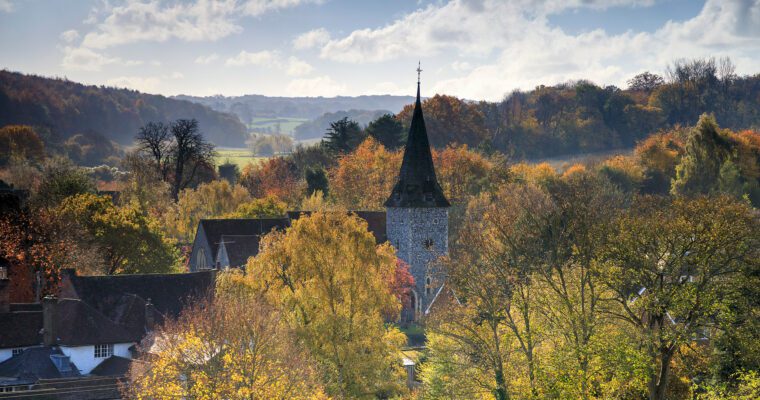 Autumn landscape, across church and houses. Trees in foreground and distance.