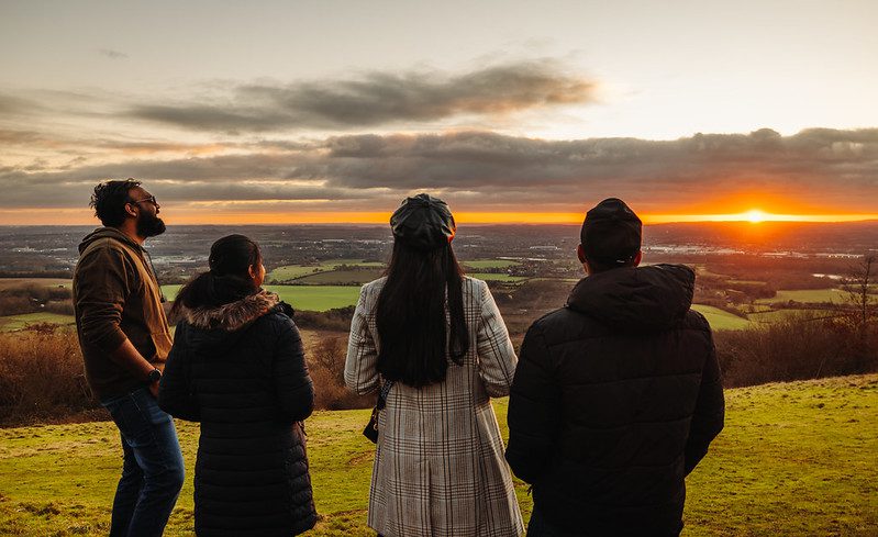 Four people watch the sunset over the countryside