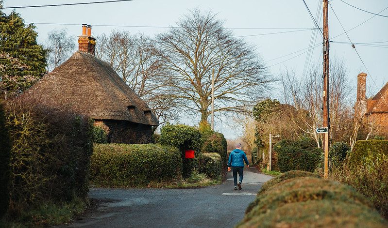 Man walking down a country lane with a thatched cottage and overhead cables