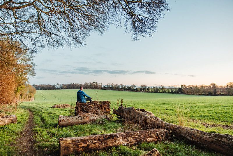 Man in a blue coat sits on a felled log in a field