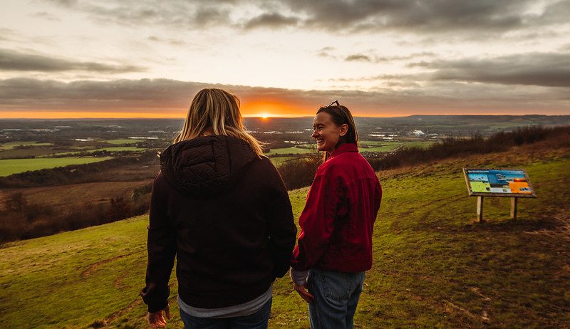 Two women smiling watch the sunset over the countryside