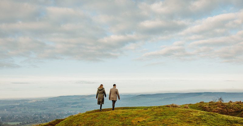 A man and woman walking away on a hill with panoramic views of countryside all around