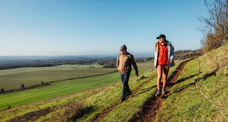A smiling man and woman walking along a countryside path with far reaching views behind