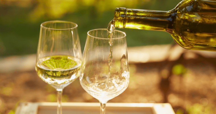 Two glasses of white wine with bottle pouring