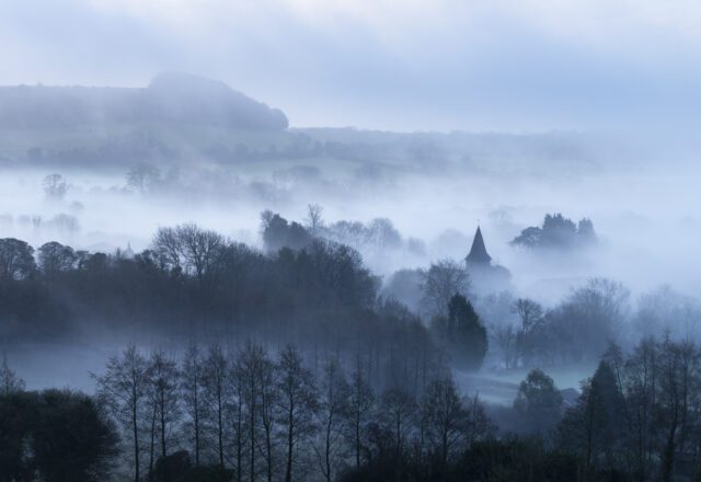 Foggy landscape, with some trees and landmarks showing through the mist.