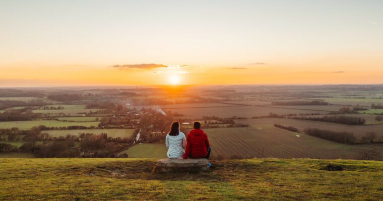 A couple sitting on the Downs watching the sunset over the countryside