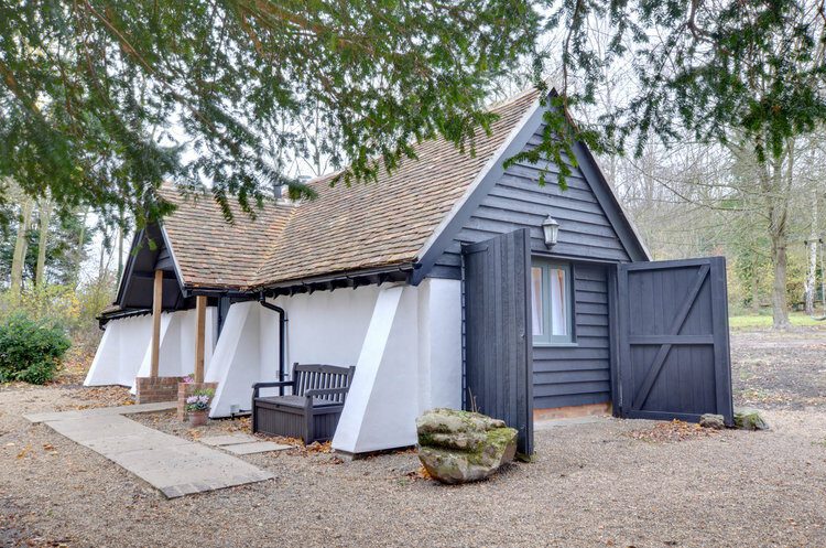 Single storey white and grey holiday home. Gravel and trees surrounding: The Snuggery.