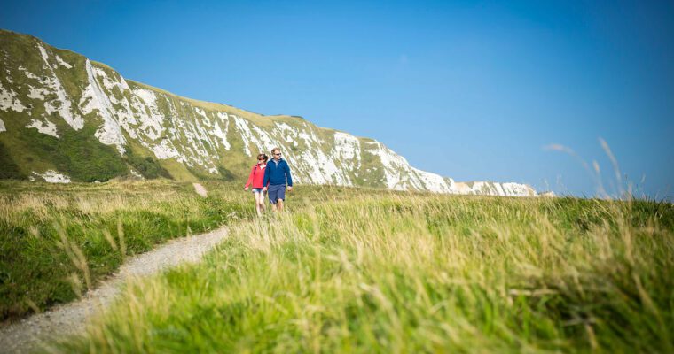 Couple walking in grassland beneath white cliffs of Dover