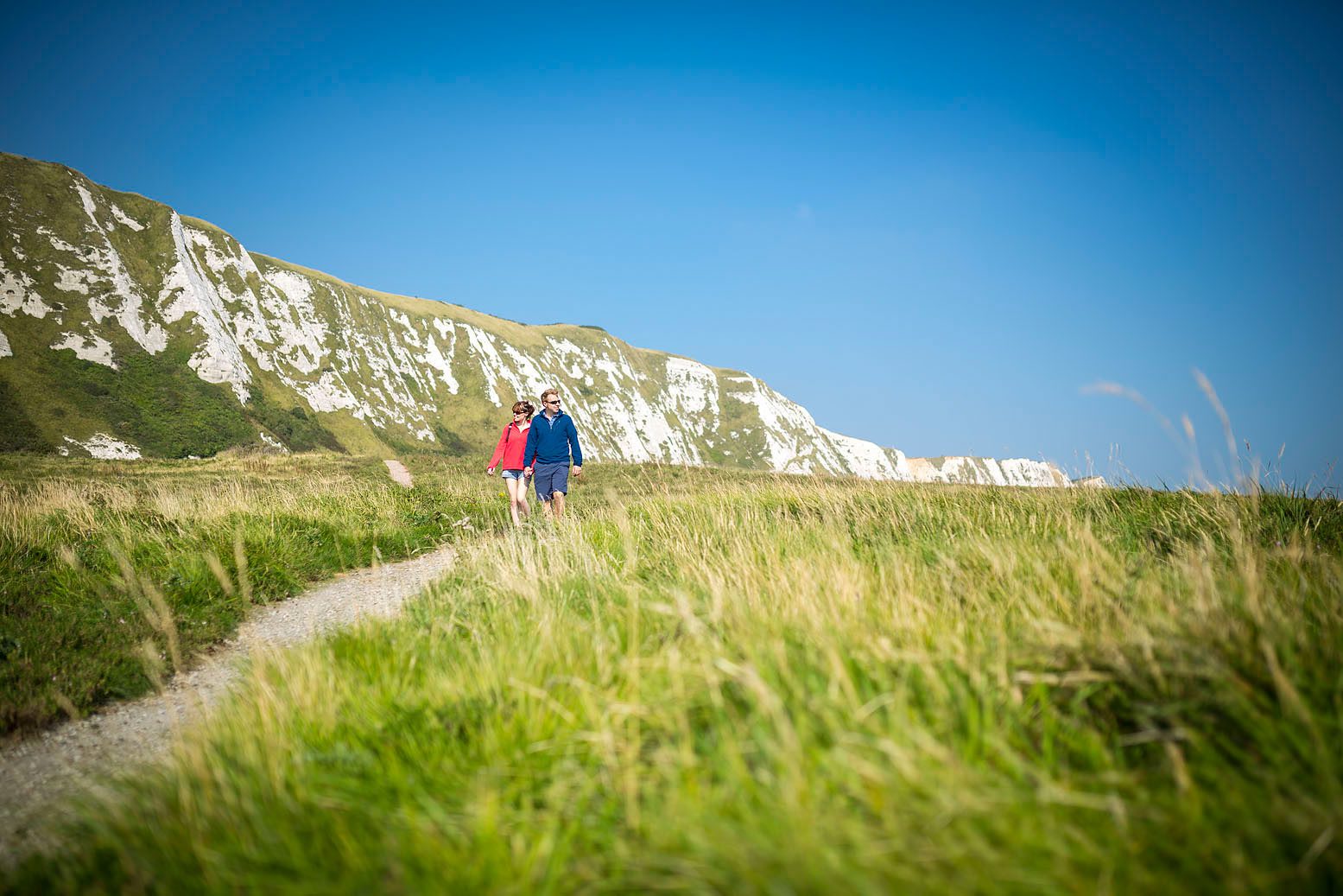 Couple walking in grassland beneath white cliffs of Dover