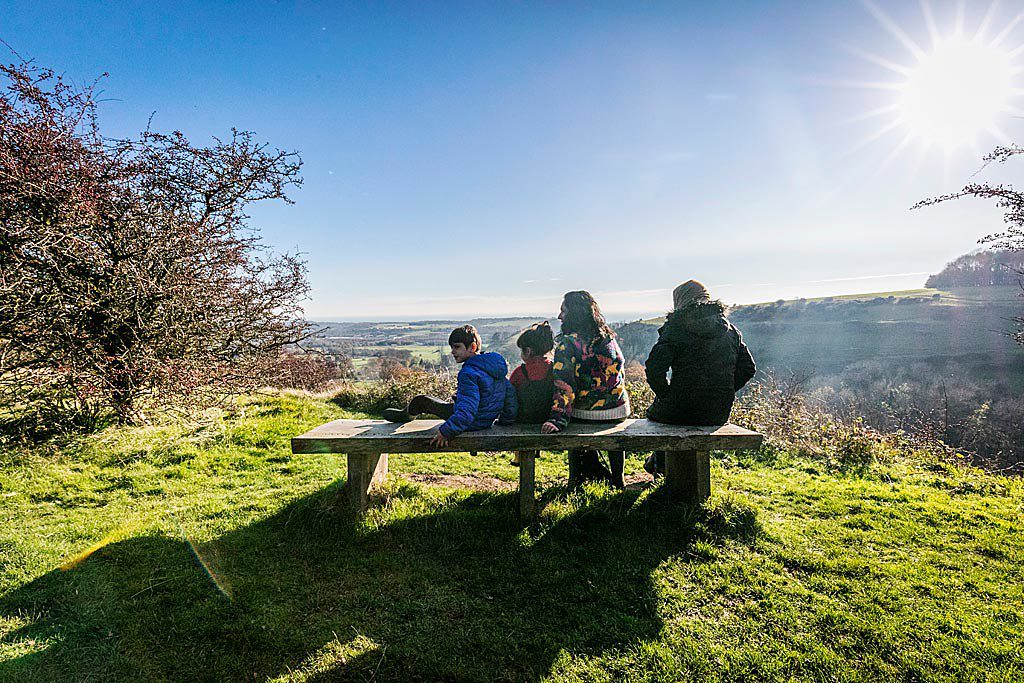 Family sitting on a carved wooden bench admiring panoramic views of the landscape