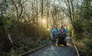 Two women and girl in wheelchair walking along footpath in winter